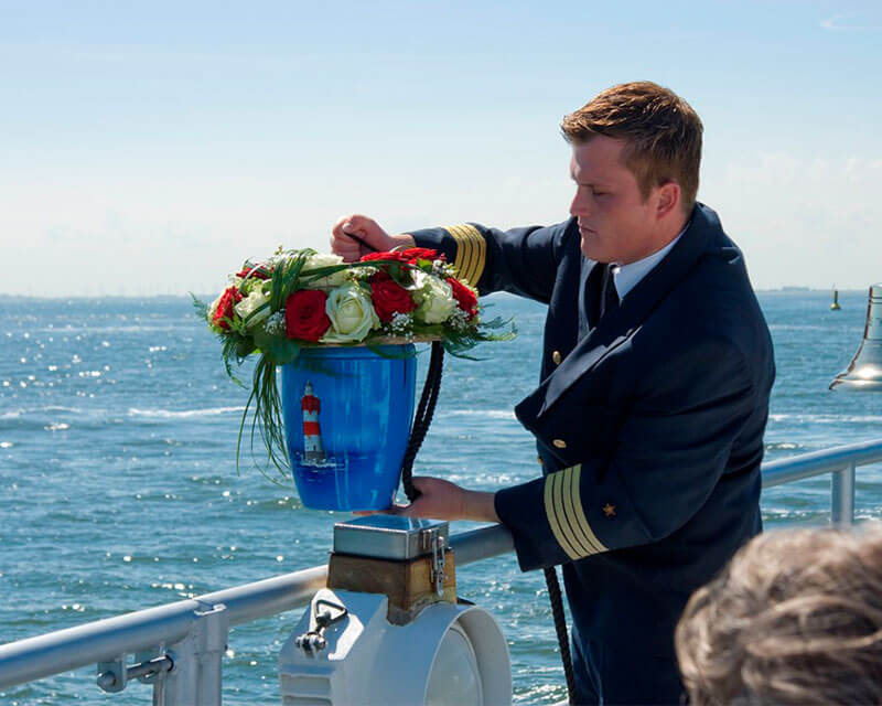 Kapitän übergibt bei einer Seebestattung die Urne mit Blumenschmuck dem Meer