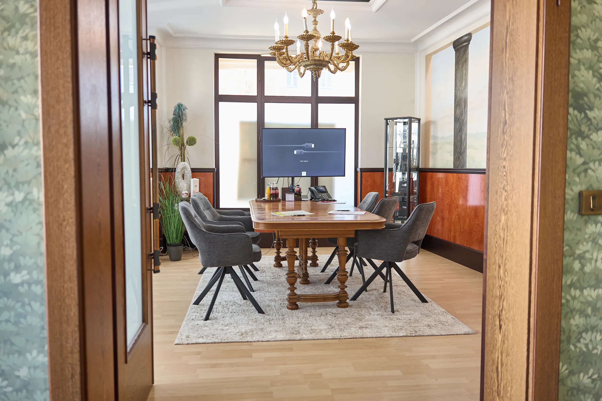 Blick durch die Tür ins Beratungszimmer in Landshut mit Kronleuchter, Holztisch und großem Monitor